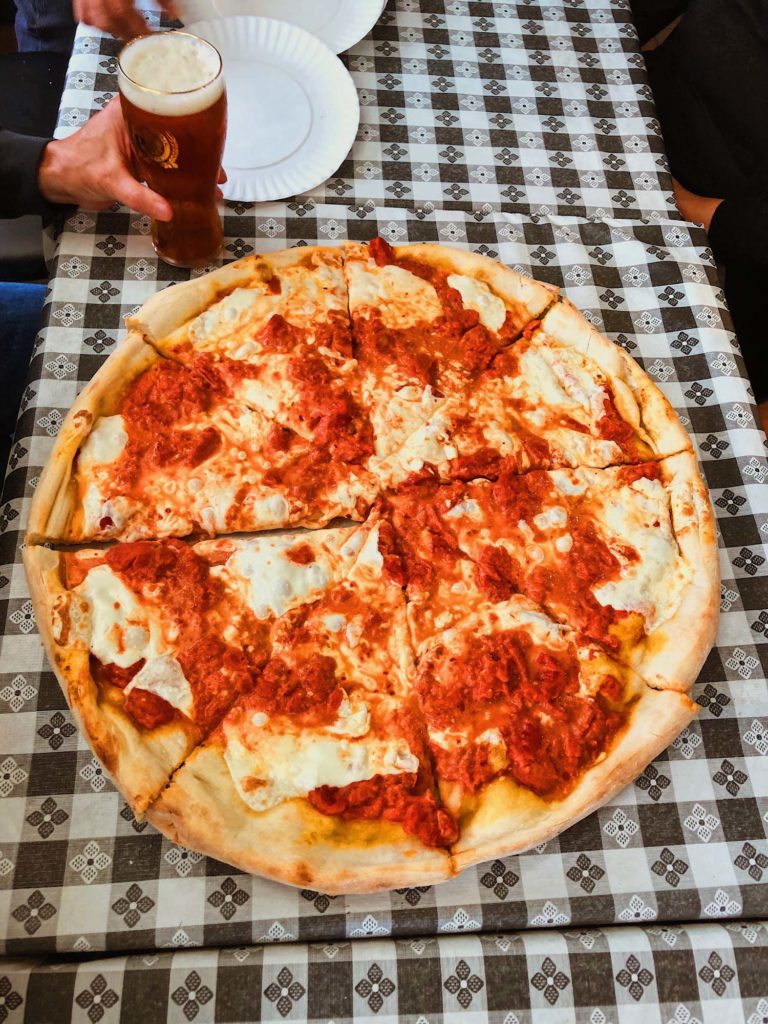 Image of a vodka sauce pizza with beer in the background