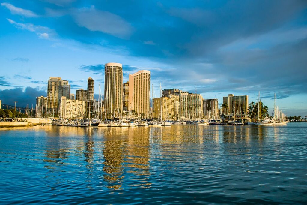 Wide angle shot of downtown Honolulu from across the water. The sky is a deep blue and the water is crisp and reflects the buildings very clearly.